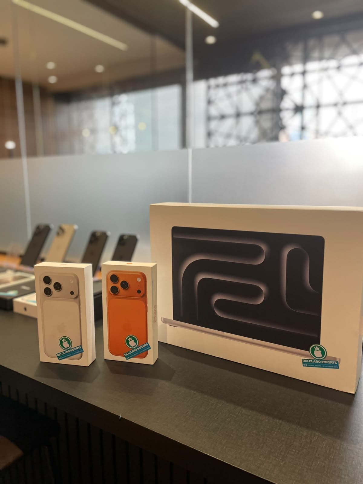 Balcão da loja com caixas de iPhone e de MacBook, e a vitrine de aparelhos ao fundo