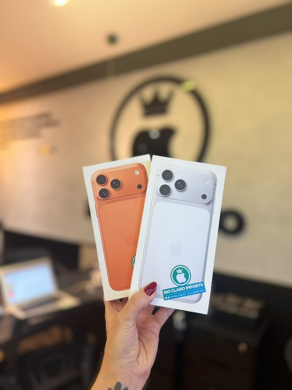 Caixas de iPhone laranja e branca diante da parede com o logo da Rio Claro Imports