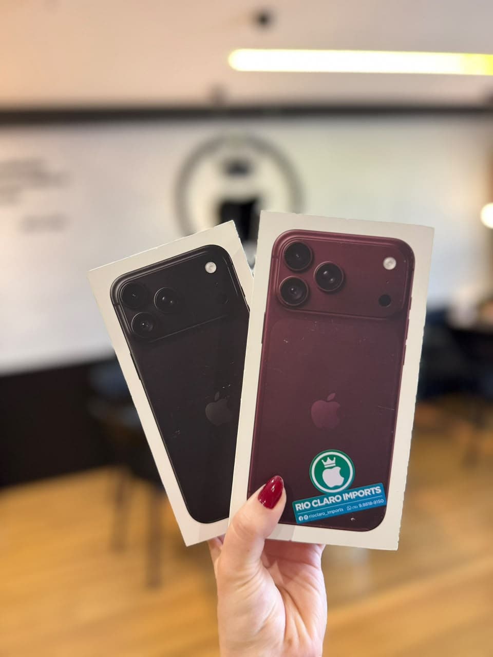 Caixas de iPhone preto e vinho com o logo da loja ao fundo